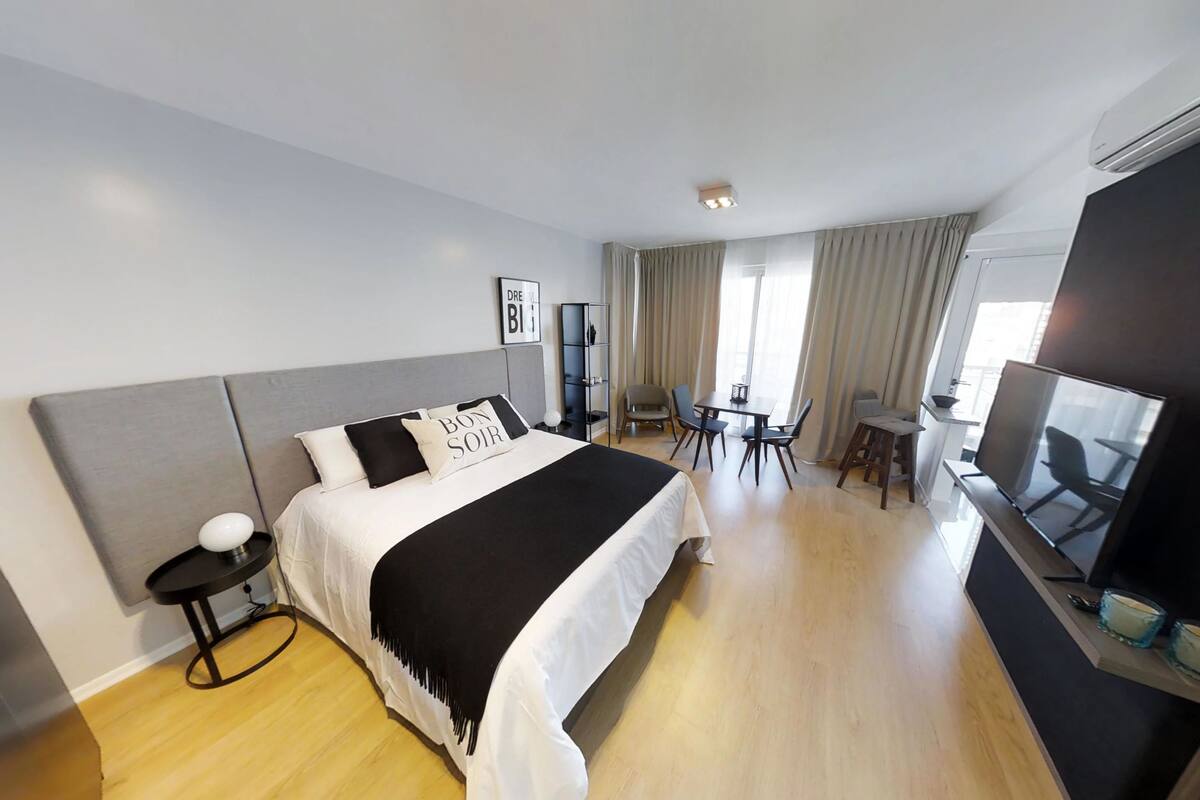 A modern hotel room with a large bed, a desk, a chair, a TV, and a wardrobe.
