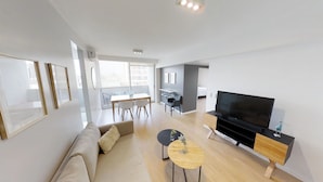 A modern living room with a sofa, a TV, and a dining area with chairs and a table. - ResidenceGV (Buenos Aires)