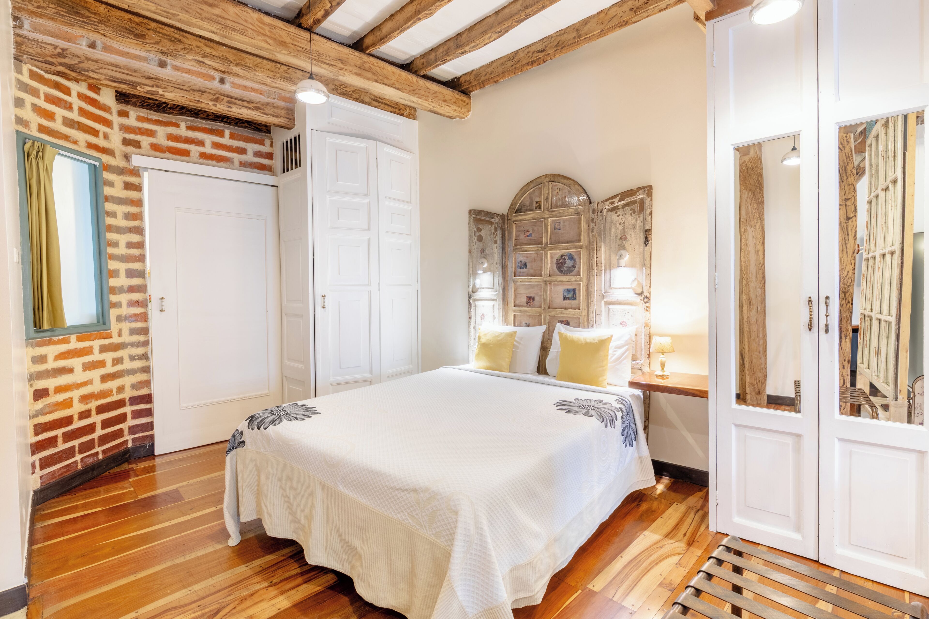 Un dormitori amb un llit gran, sòl de fusta, paret de maó i una porta blanca.
