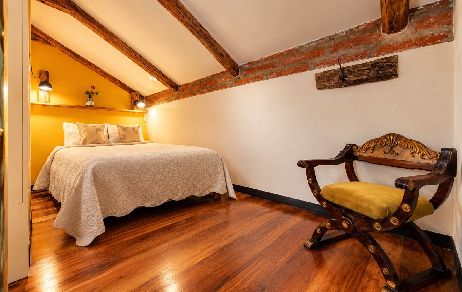 A bedroom with a bed, a wooden chair, and a brick wall.