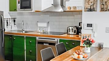 Une cuisine moderne avec des meubles de couleur verte, une table à manger en bois et un vase rempli de fleurs.