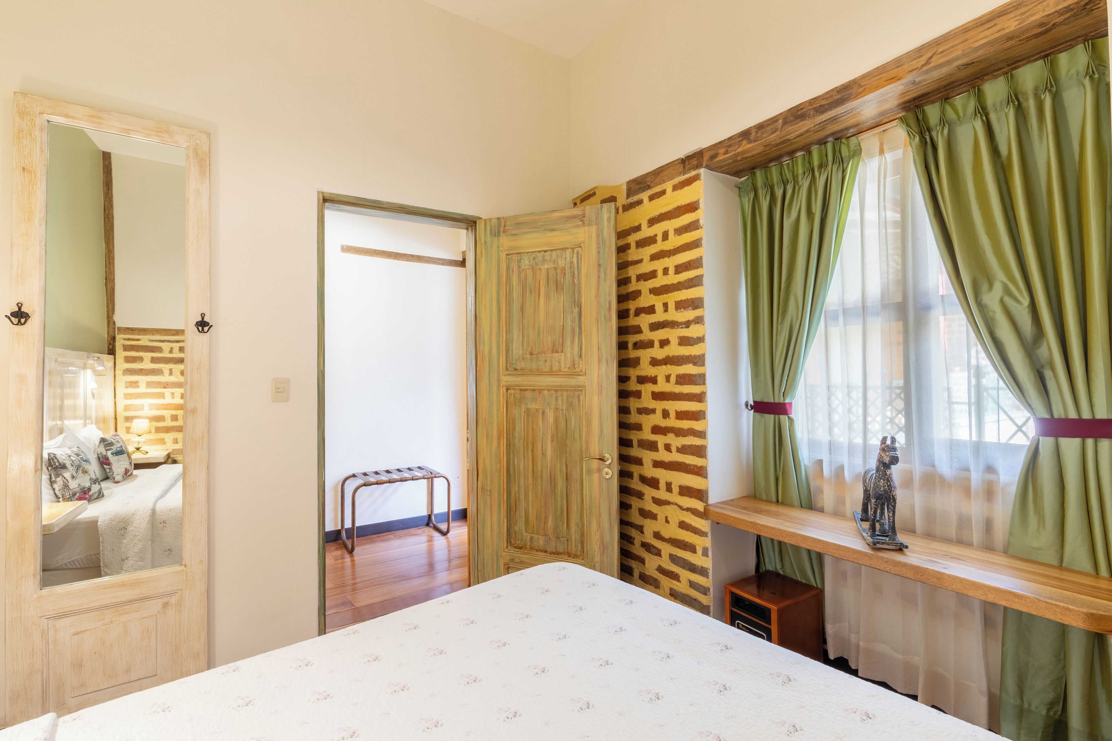 Une chambre à coucher avec un lit, une porte en bois, un mur en briques et une fenêtre avec des rideaux verts.