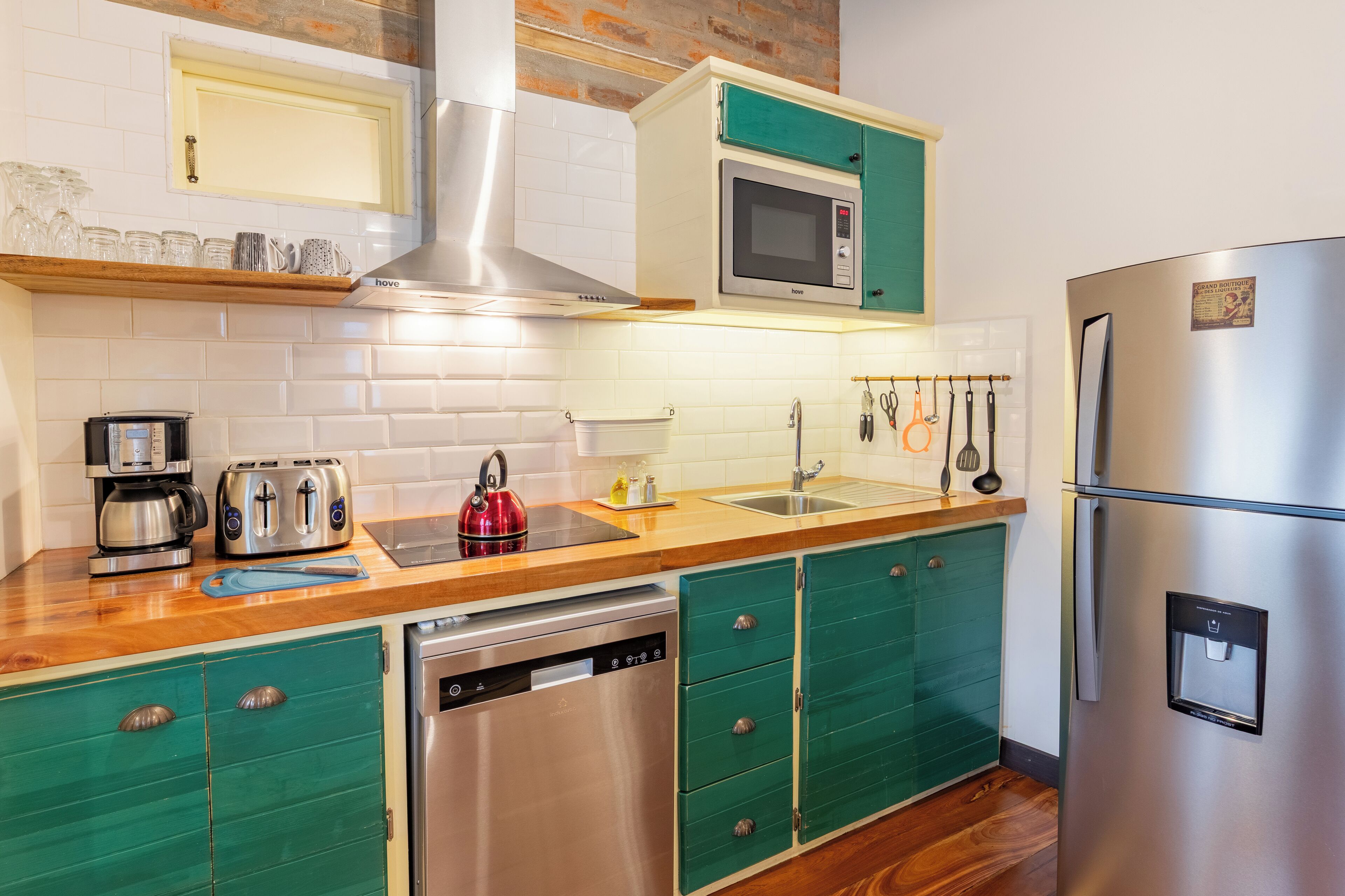 Una cocina moderna con un refrigerador de acero inoxidable, un microondas, un lavavajillas y una tetera.