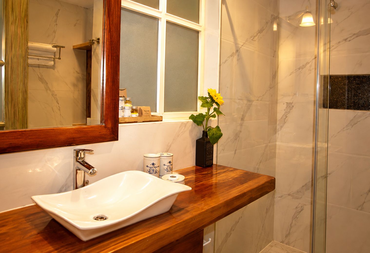 Une salle de bain avec un lavabo en marbre, un meuble-lavabo en bois, un miroir, une fenêtre et un espace douche.