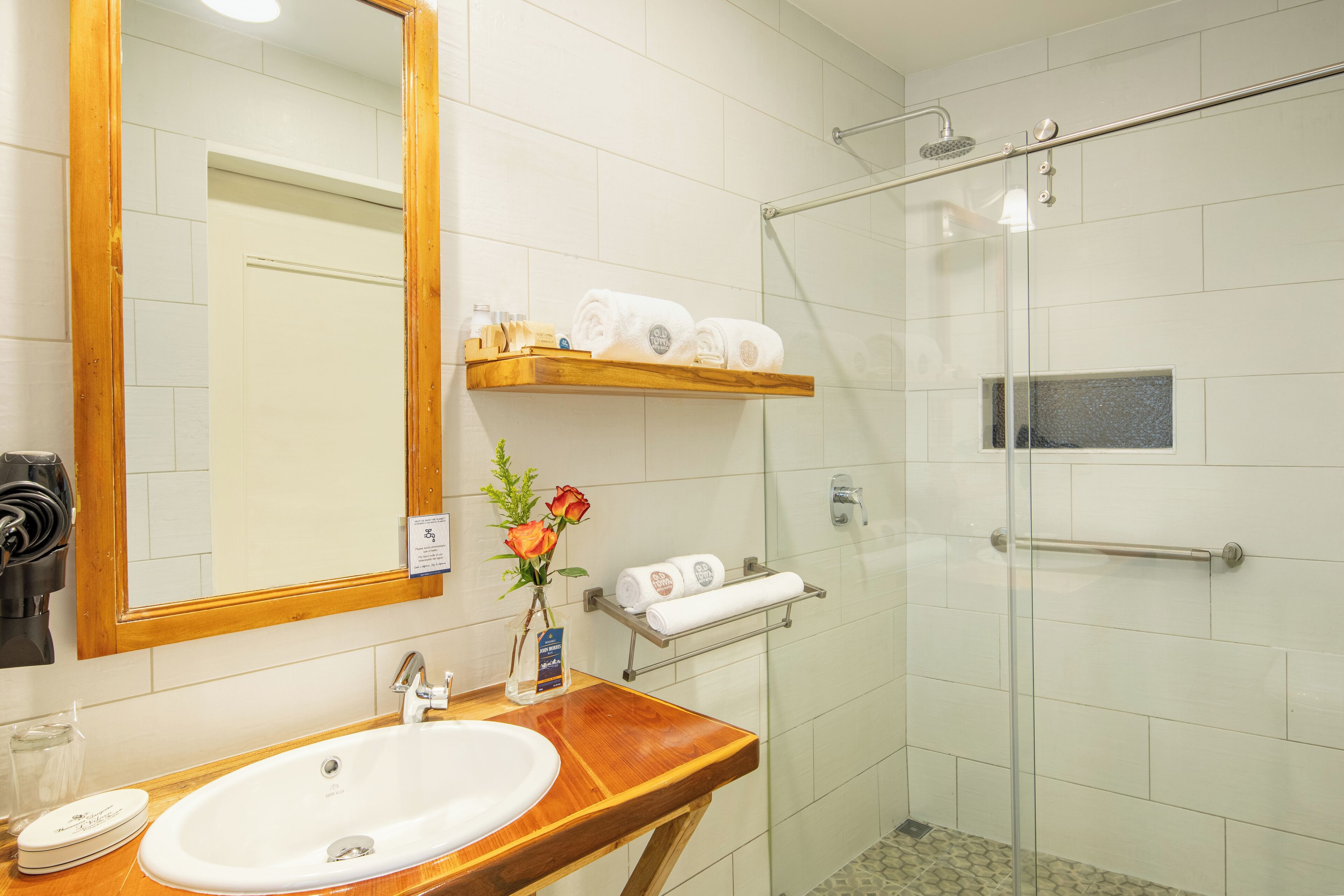 A bathroom with a wooden vanity, a sink, a mirror, a glass shower enclosure, and a towel rack.