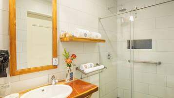 A bathroom with a wooden vanity, a sink, a mirror, a glass shower enclosure, and a towel rack.