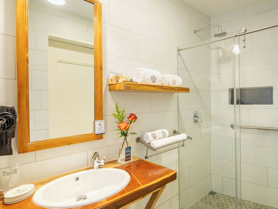 A bathroom with a wooden vanity, a sink, a mirror, a glass shower enclosure, and a towel rack.