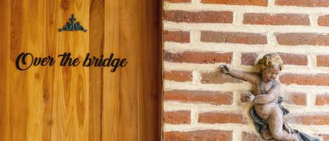 Una puerta de madera con la inscripción “Over the bridge” y un muro de ladrillo con una estatua de un ángel.