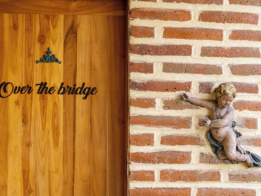 Una puerta de madera con la inscripción “Over the bridge” y un muro de ladrillo con una estatua de un ángel.