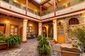 A spacious courtyard with stone flooring, multiple seating areas, and a variety of potted plants.