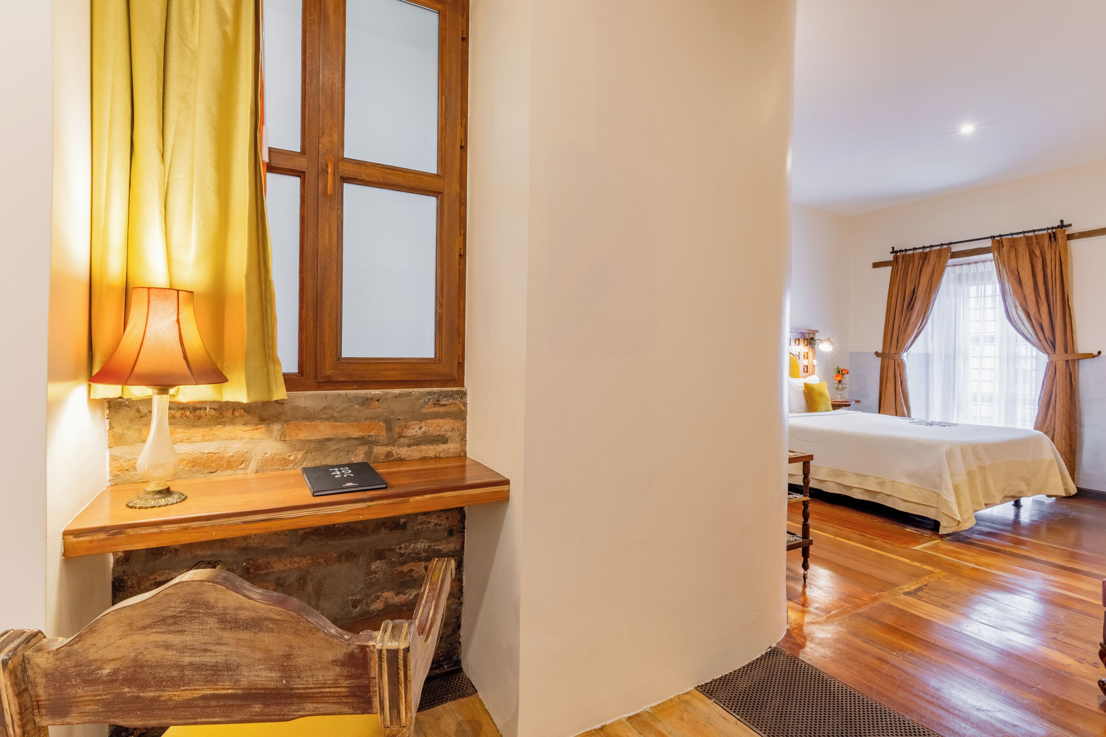 Une chambre avec un bureau en bois, un lit recouvert d’une courtepointe blanche et une fenêtre avec des rideaux.