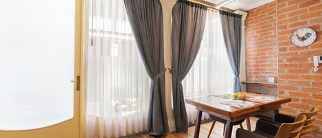 A room with a wooden floor, a dining table with chairs, a clock on the wall, and a door with curtains.
