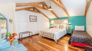A bedroom with a wooden ceiling, a bed with a patterned bedspread, a bedside table with a lamp, and a dresser with a vase of flowers.