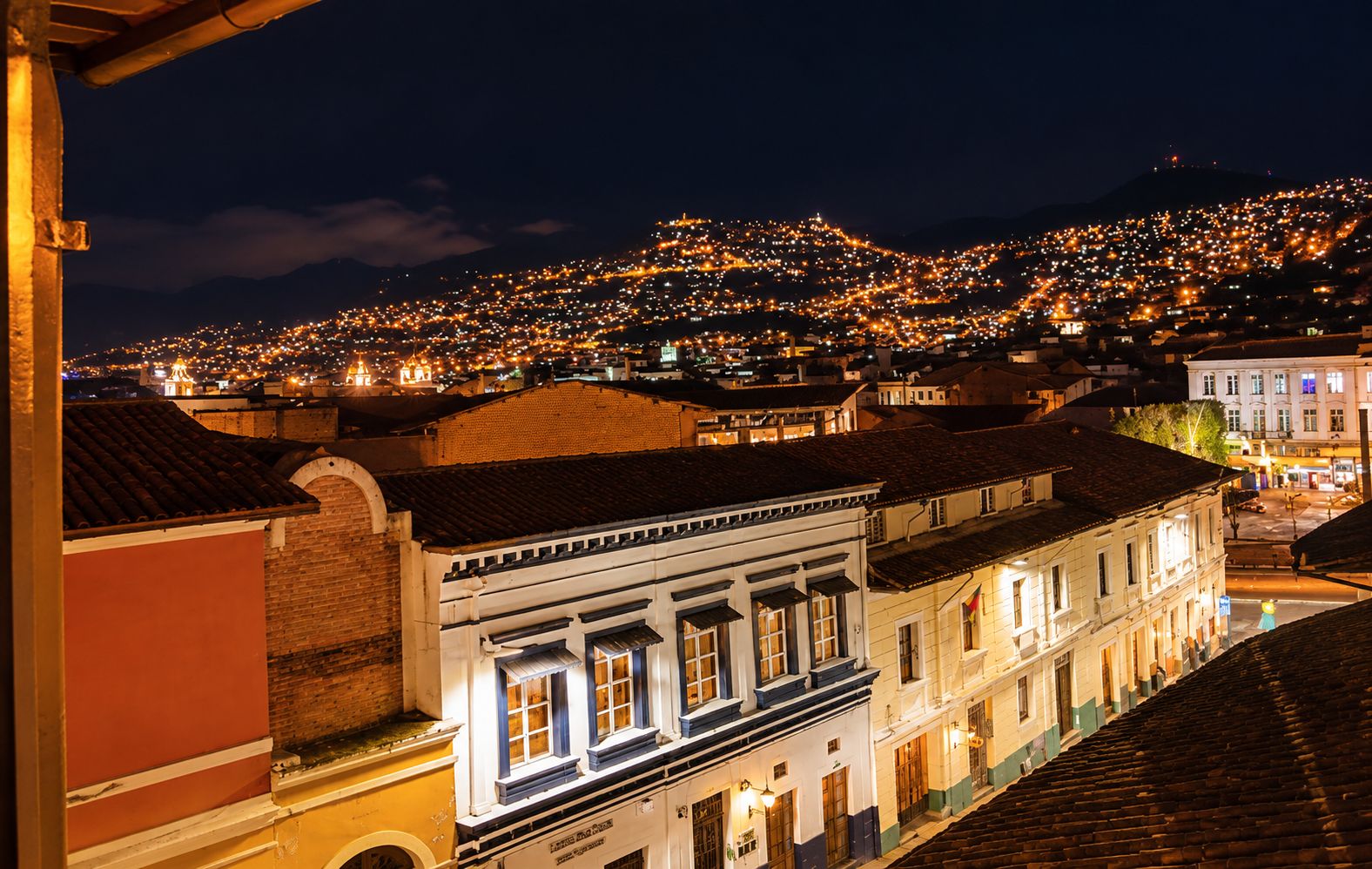 Une vue nocturne d’une ville, avec des bâtiments illuminés et une colline en arrière-plan.