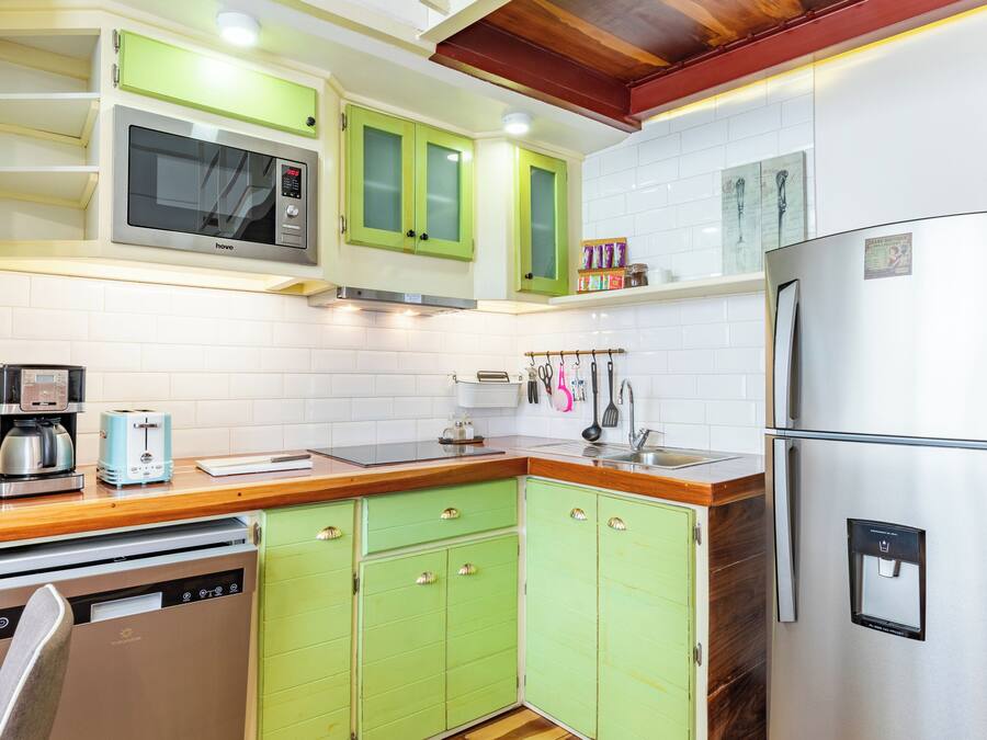 A kitchen with green cabinets, a stainless steel refrigerator, a built-in microwave, a coffee maker, and a dishwasher.