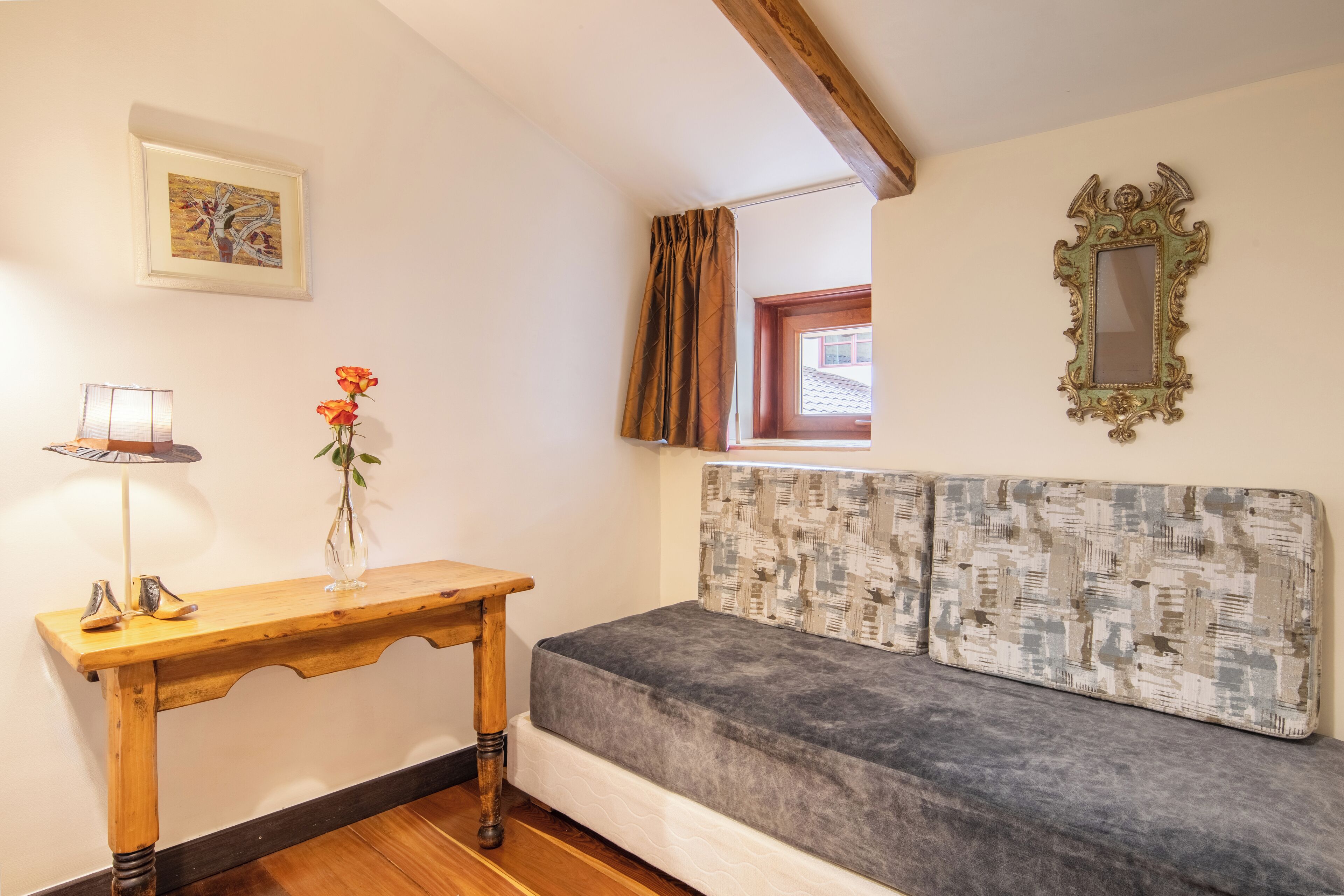 Una habitación acogedora con una mesa de madera, un florero con flores, un cabecero estampado y un espejo enmarco.