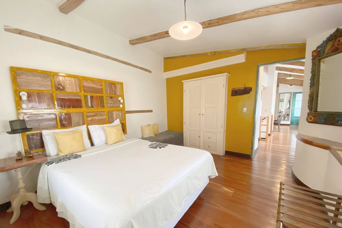 A bedroom with a large bed, wooden beams, a white wardrobe, and a mirror with a decorative frame.