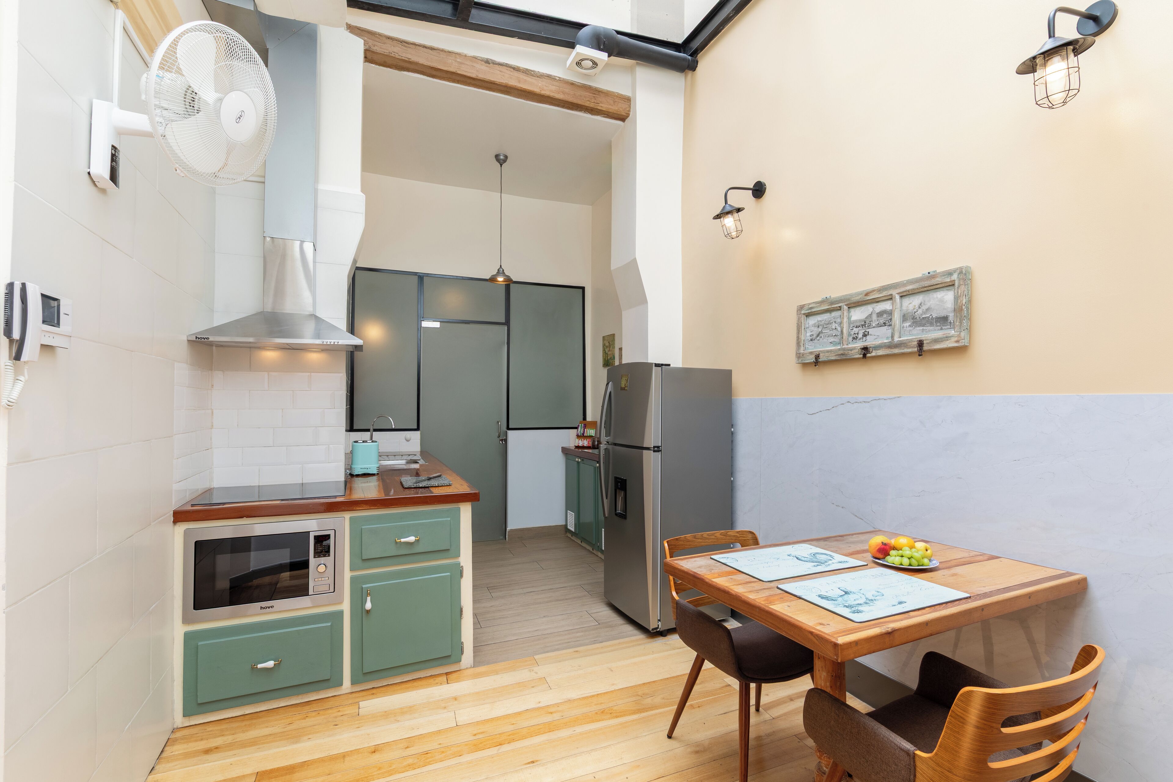 A compact kitchen with a dining area, a built-in oven, a microwave, a fan, and a refrigerator.