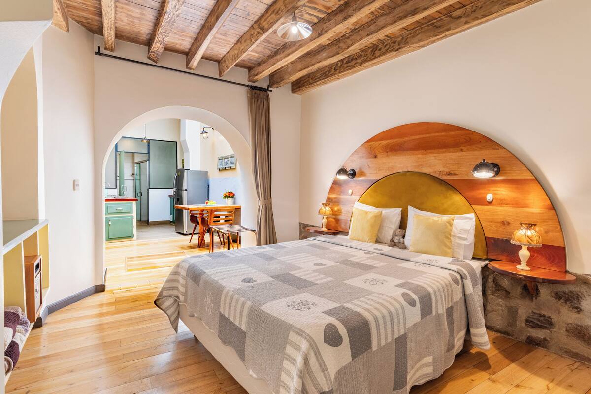 A bedroom with a large bed, wooden headboard, and a small table with a lamp.