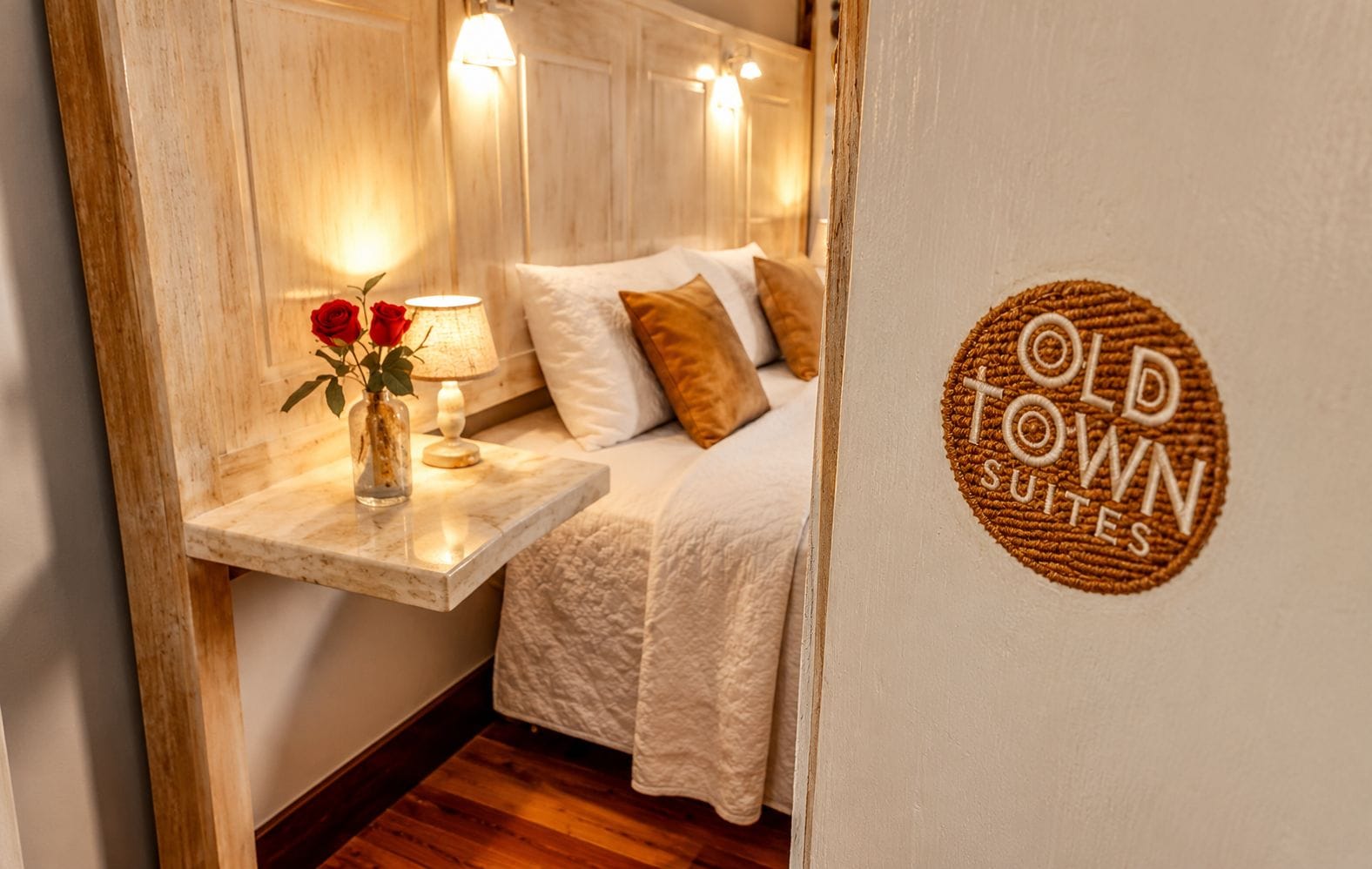 A bedroom with a bed, pillows, a nightstand with a lamp, and a vase with flowers.
