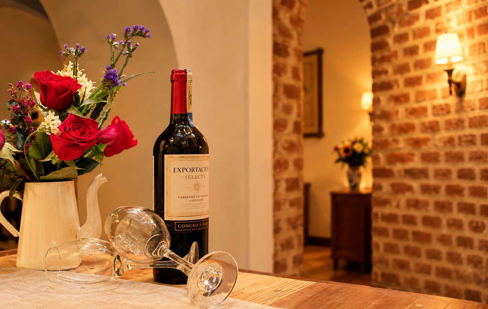 Una botella de vino, una copa y un florero con flores sobre una mesa.