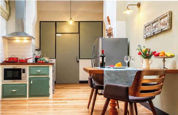 A compact kitchen with a microwave, stove, and cabinets, a dining area with a table and chairs, and a refrigerator.