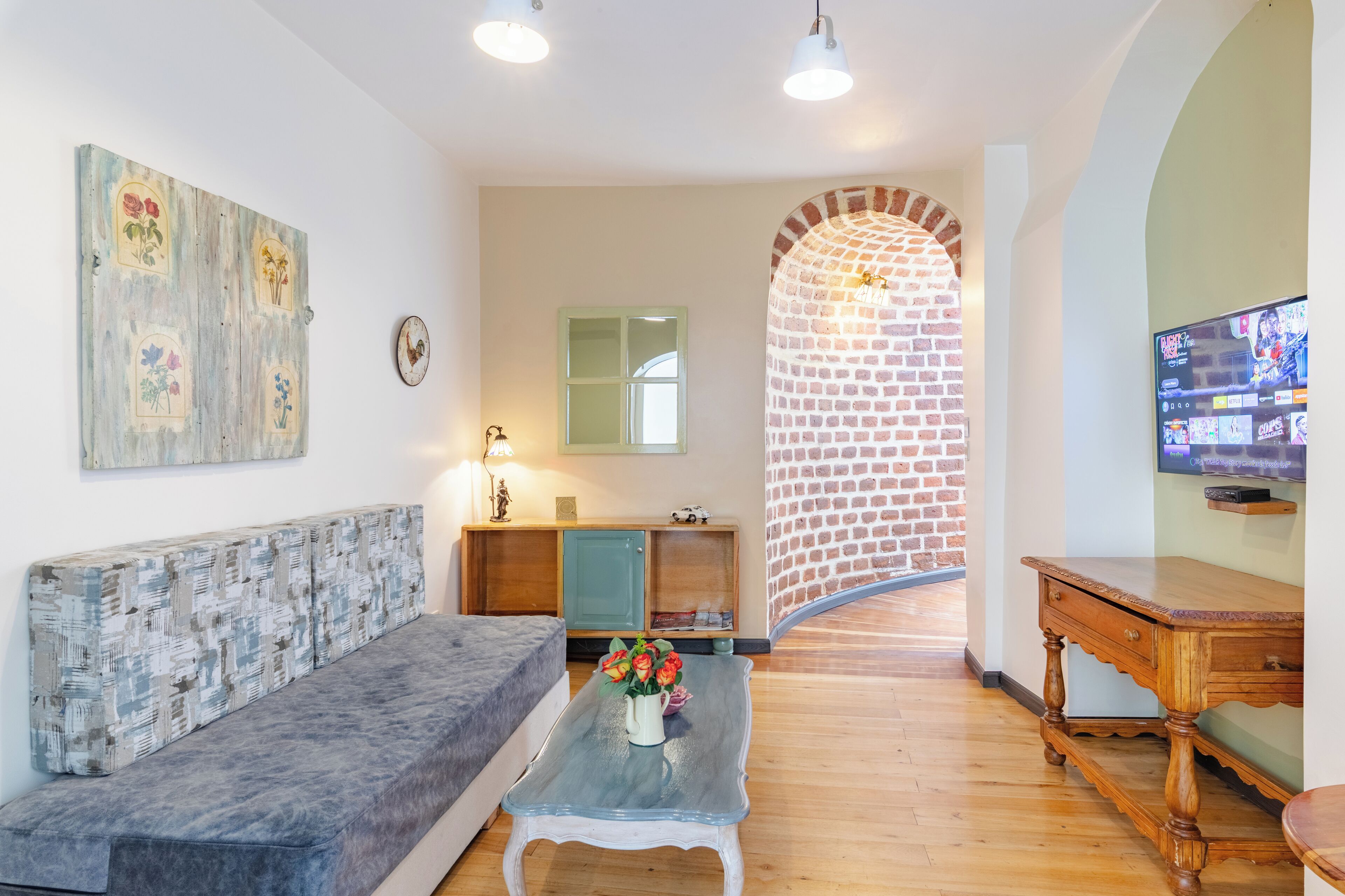 A living room with a sofa, a coffee table with flowers, a TV, and a brick wall arch.