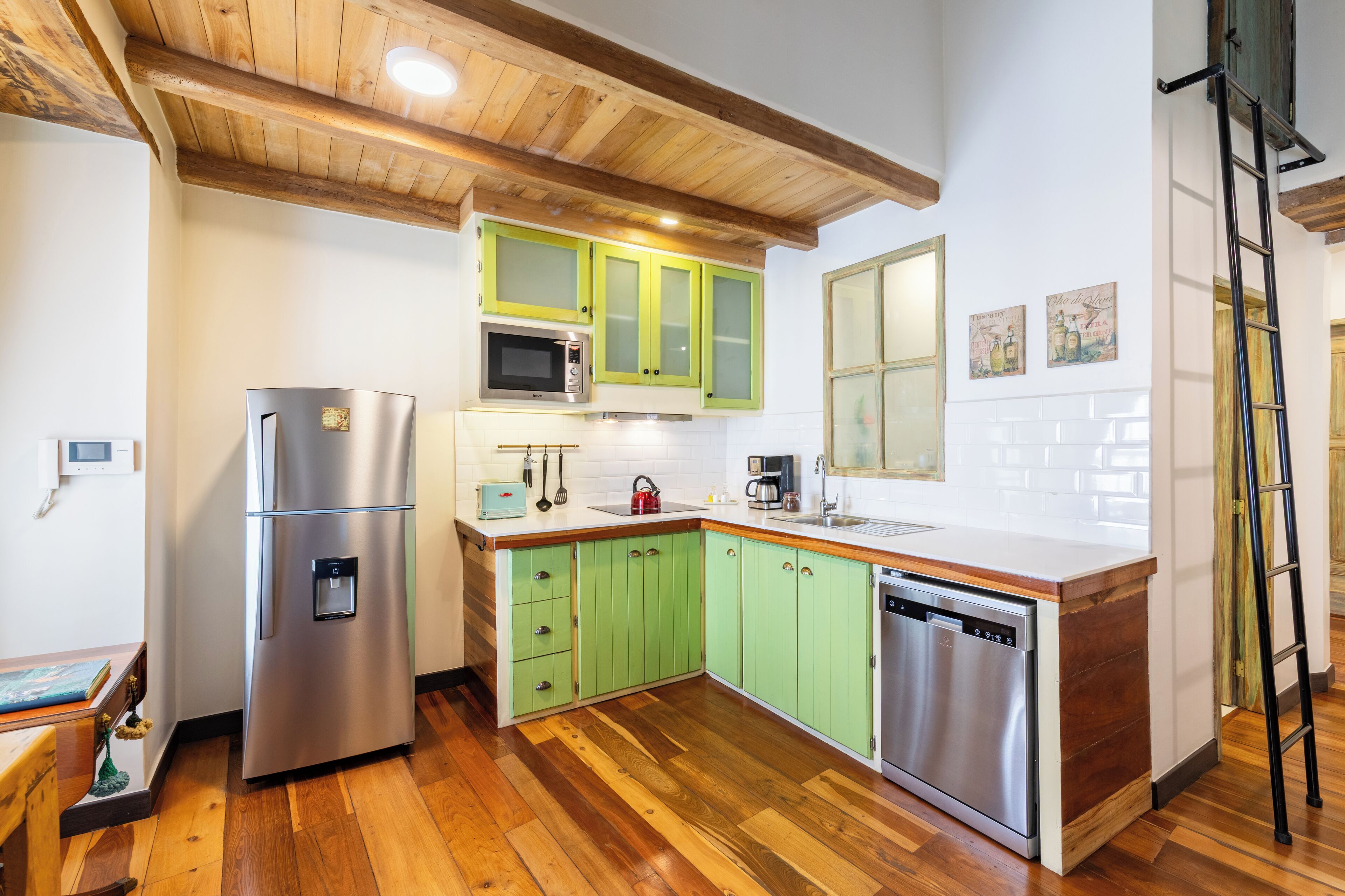 Une cuisine de taille réduite avec des meubles verts, des appareils en acier inoxydable et un plancher en bois.