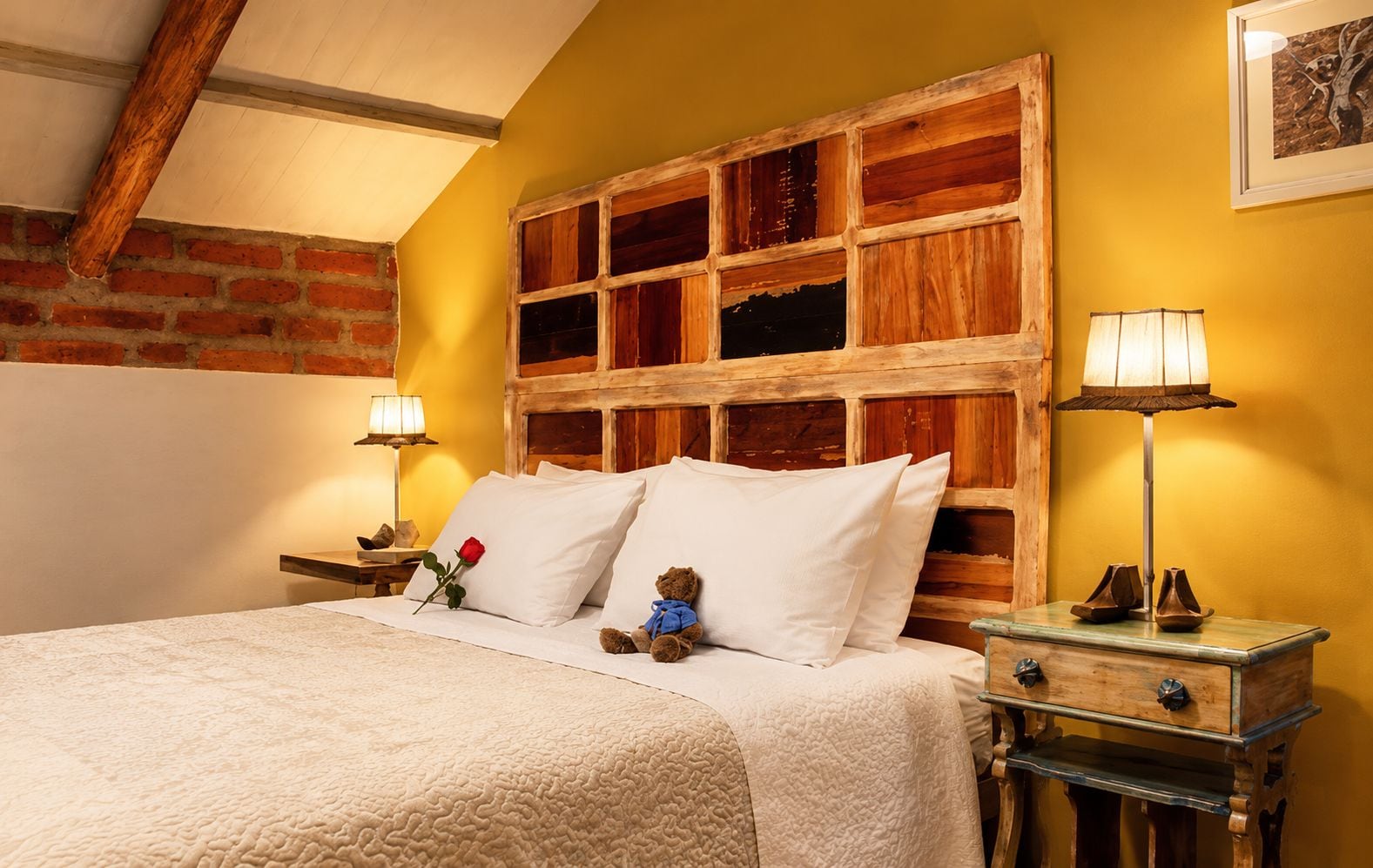 Un lit avec une literie blanche, une tête de lit en bois, deux lampes de chevet, une petite table avec une lampe et un ours en peluche.