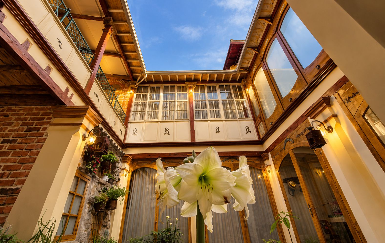 L’intérieur d’un hôtel avec un atrium central, des poutres en bois, une grande fleur blanche et une vue sur le ciel à travers le toit.