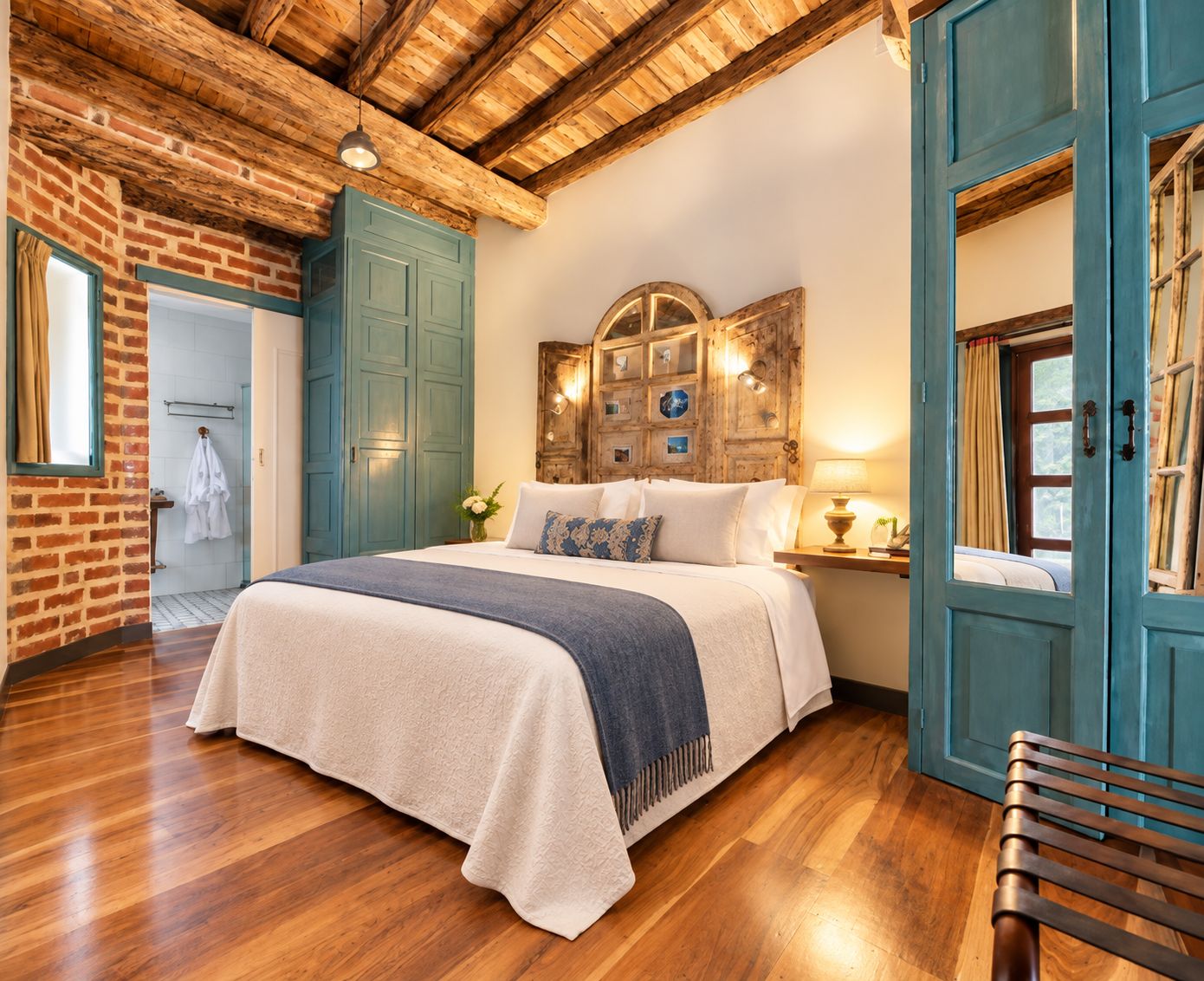 A bedroom with a wooden ceiling, a bed with a blue and white bedspread, a wooden nightstand with a lamp, and a blue door.