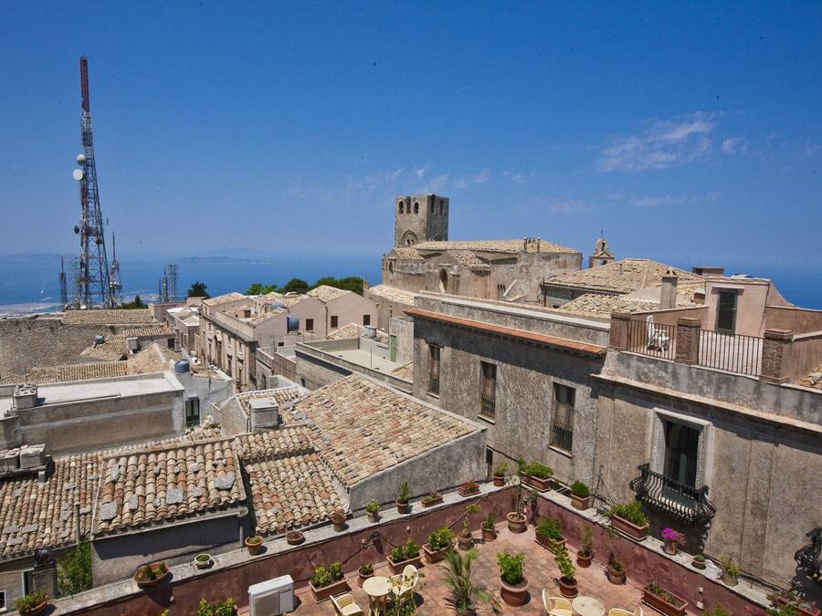 Un pueblo histórico con edificios de tejados de terracota, una torre destacada y una vista despejada del mar.