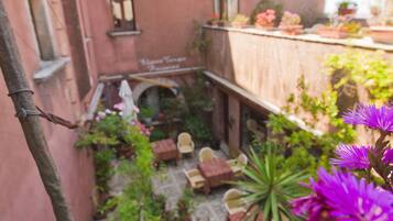 Un patio con un edificio rosa, plantas en macetas y flores moradas.