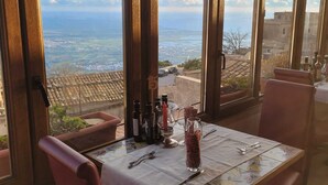 A dining table with a view of a coastal landscape through large windows. - Hotel Elimo (Erice)