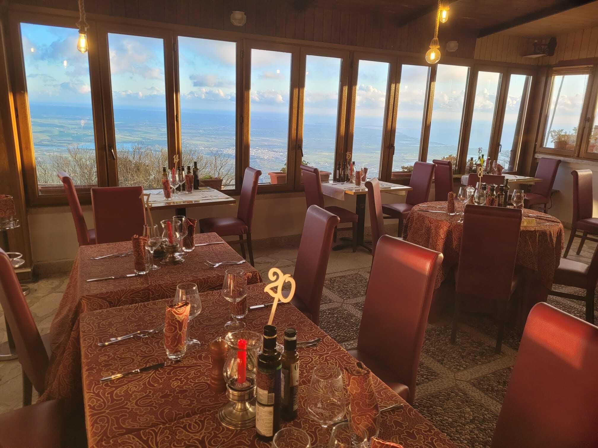 A restaurant with tables set for dining, large windows offering a view of the landscape, and hanging light fixtures.