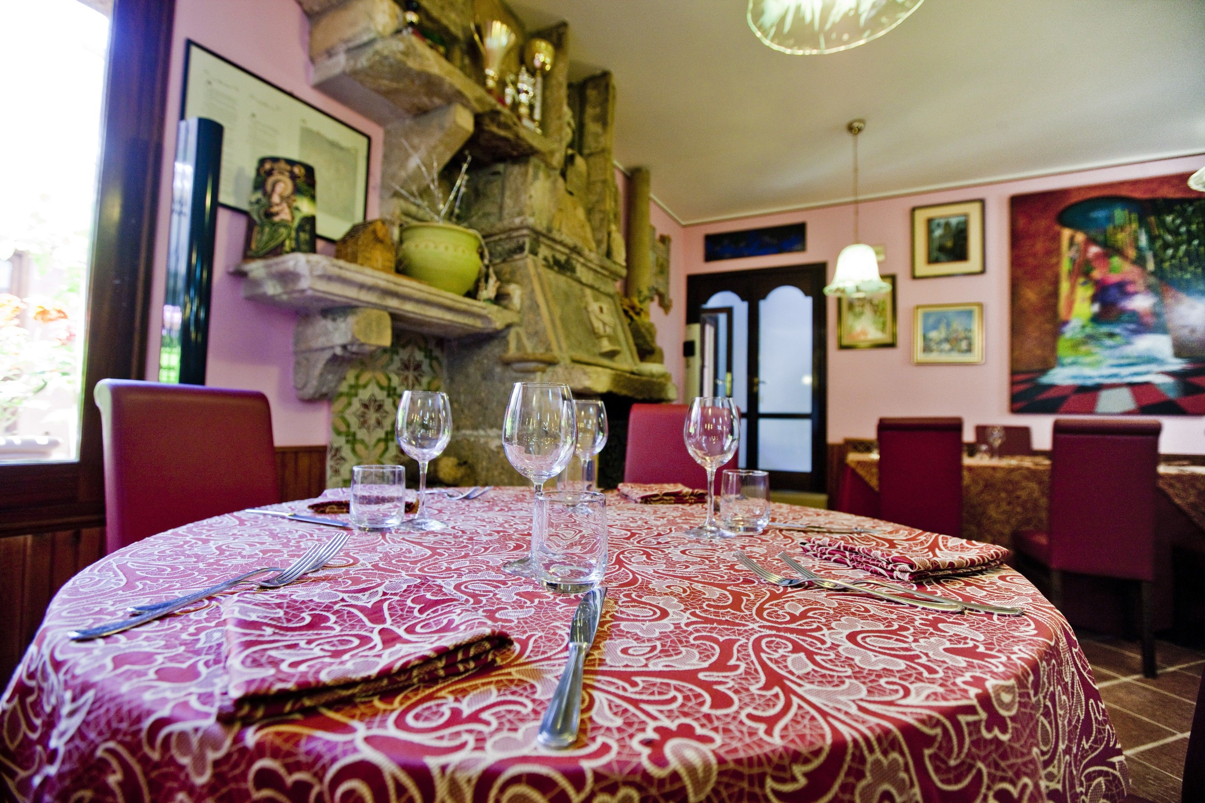 A dining table set with wine glasses, cutlery, and a patterned tablecloth in a room with a stone wall and artwork.