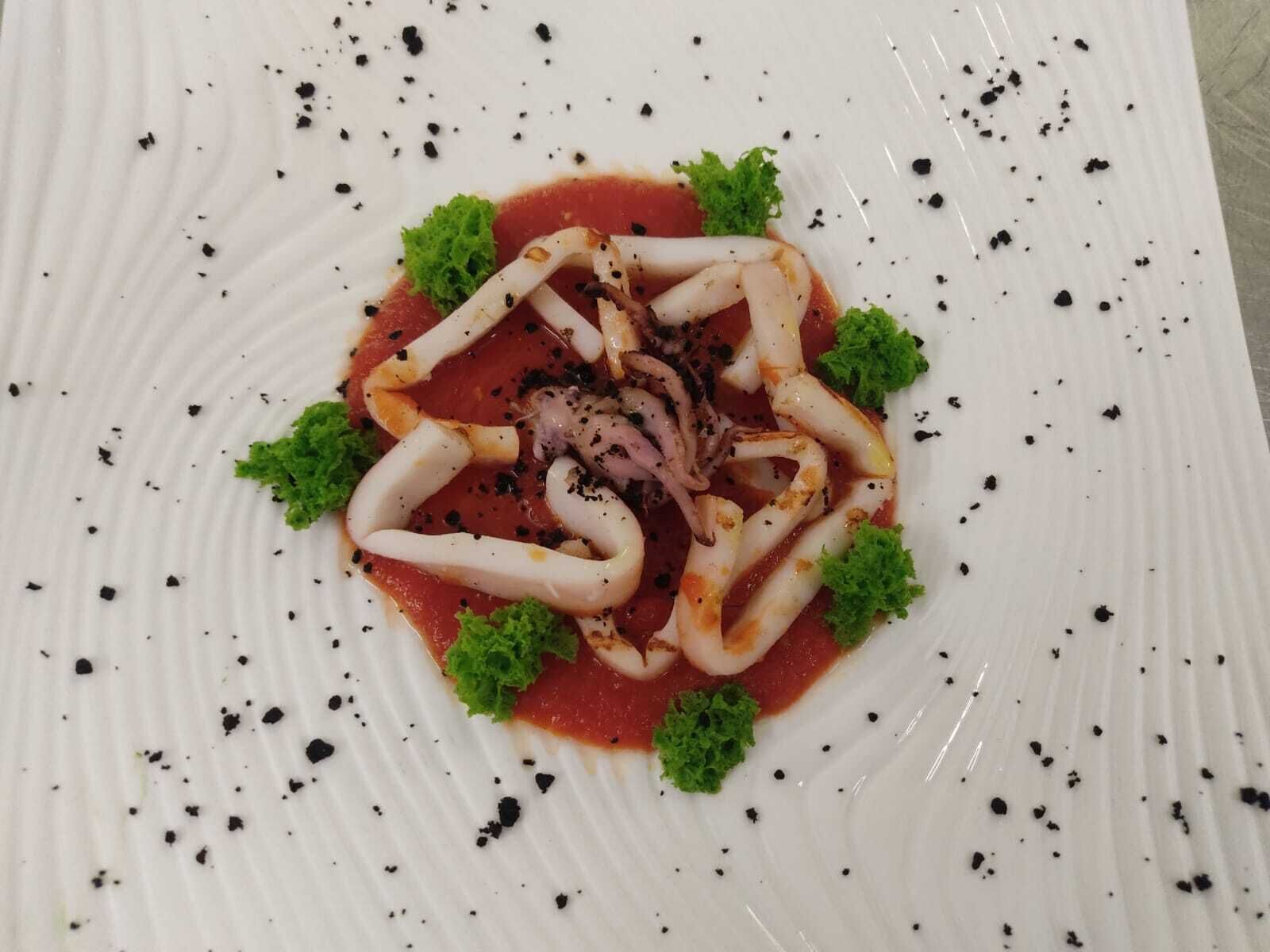 Un plato de comida con calamares dispuestos en un círculo, adornado con hojas verdes y motas negras.
