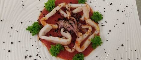 Un plato de comida con calamares dispuestos en un círculo, adornado con hojas verdes y motas negras.