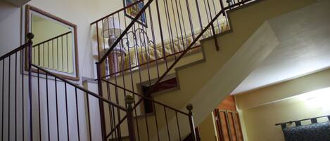 A staircase with a metal railing, a mirror on the wall, and a bed with a patterned cover.