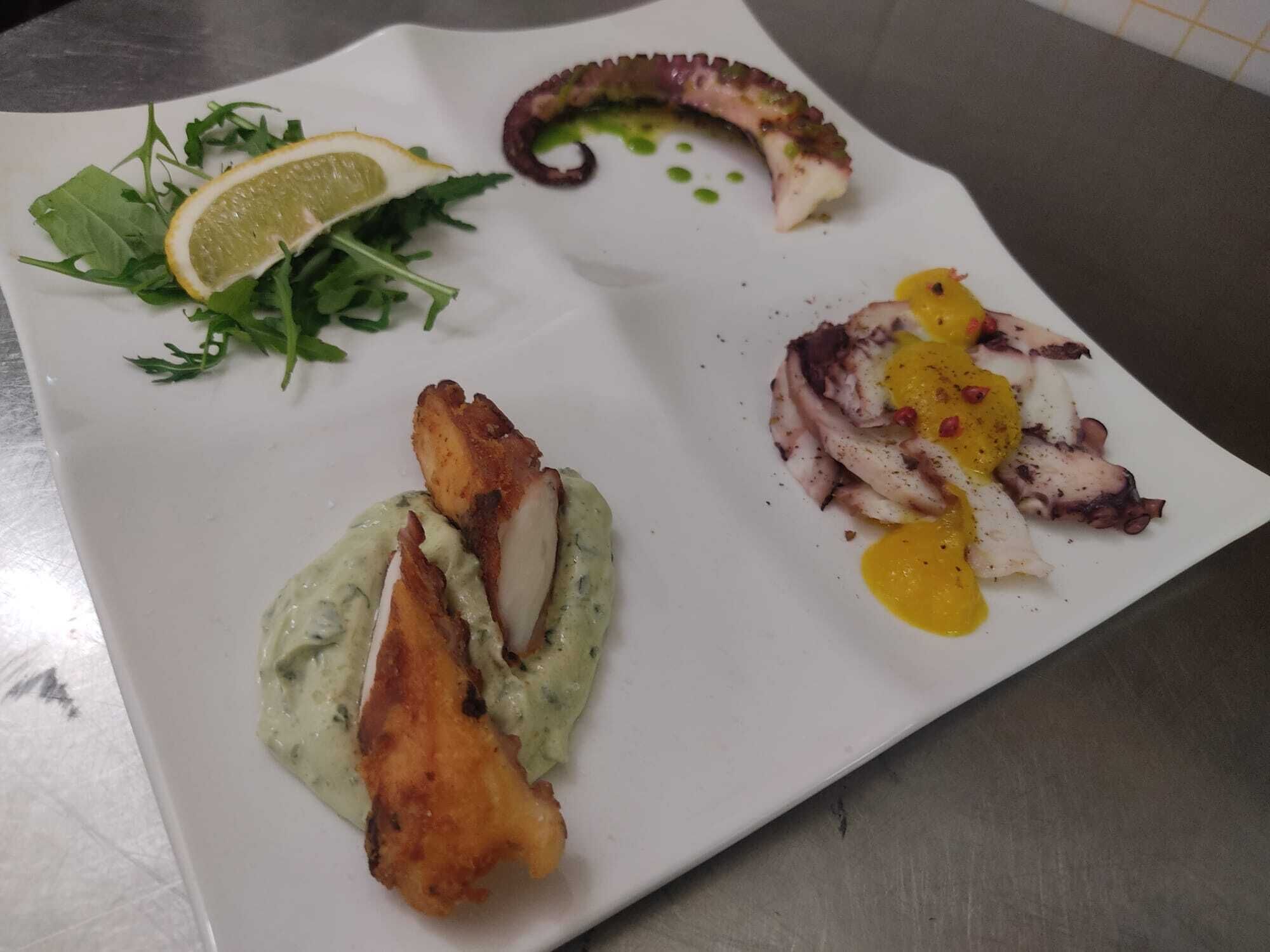 A white plate with octopus, lemon, greens, and a creamy sauce.