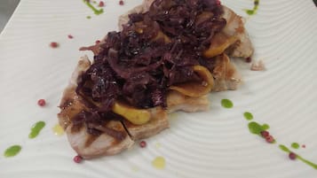 A plate with a dish topped with red cabbage and slices of apple, garnished with green and yellow sauces.