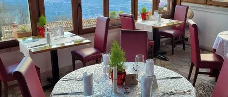A restaurant with round tables, red chairs, and a view of the sea.