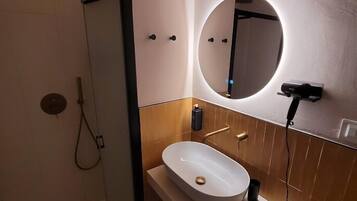 A modern bathroom with a glass-enclosed shower, a white sink with a round mirror, and a towel rack.