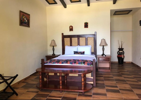 A hotel room with a large bed, two bedside tables with lamps, a bench, and a potted plant. - Cassia Hill Resort (San Ignacio)