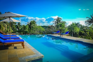 A clear blue pool with lounge chairs and umbrellas, surrounded by lush greenery and palm trees. - Cassia Hill Resort (San Ignacio)