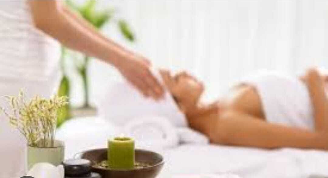 A spa setting with a person receiving a massage, a small plant, and a candle on a table.