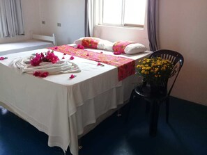 A neatly made bed with a white bedspread, pink floral pillows, and a decorative towel. A chair with a yellow flower arrangement is beside the bed. - Hostel Estrela de Maraca (Ipojuca)