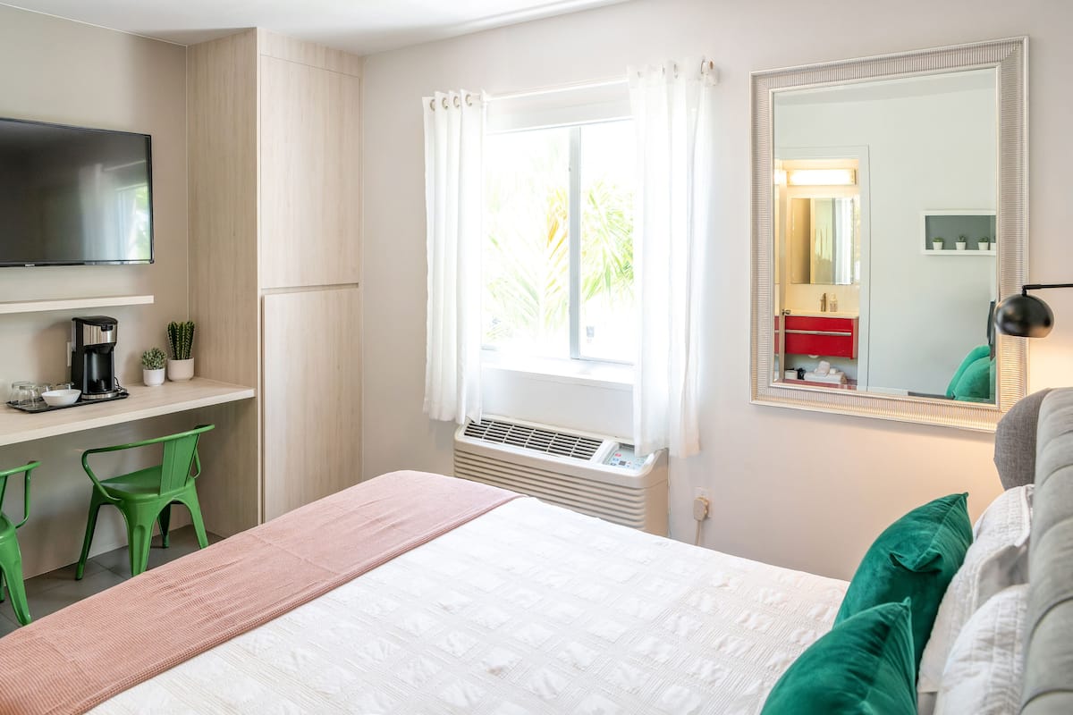 A hotel room with a bed, a desk with a chair, a TV, a window with curtains, and a mirror.