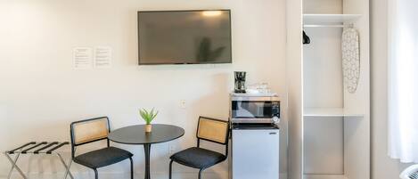 A compact hotel room with a bed, a small table with chairs, a television, a microwave, and a shower area.