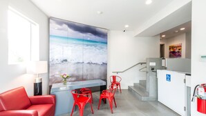 A modern hotel room with a large window, a red sofa, a dining table with red chairs, a kitchen area, and a staircase. - Costa Norte Boutique Hotel (Miami Beach)
